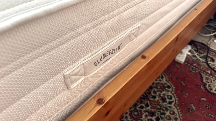 The side of the Slumberland Air 6.0 Memory mattress, on a wooden bed frame. One of the carry handles displays the Slumberland logo