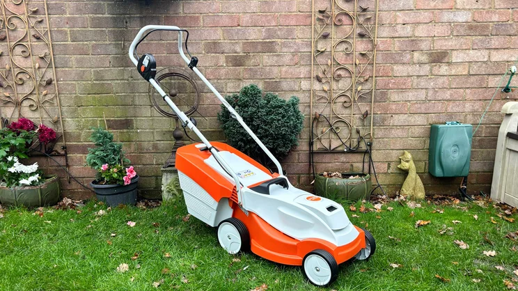 The Stihl RMA 235 lawn mower in a garden, in front of a brick wall
