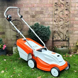 The Stihl RMA 235 lawn mower in a garden, in front of a brick wall