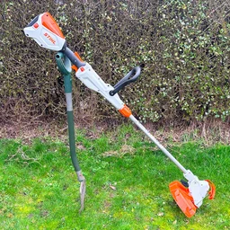 The Stihl FSA 50 grass trimmer propped upright on a spade in a garden, in front of a hedge