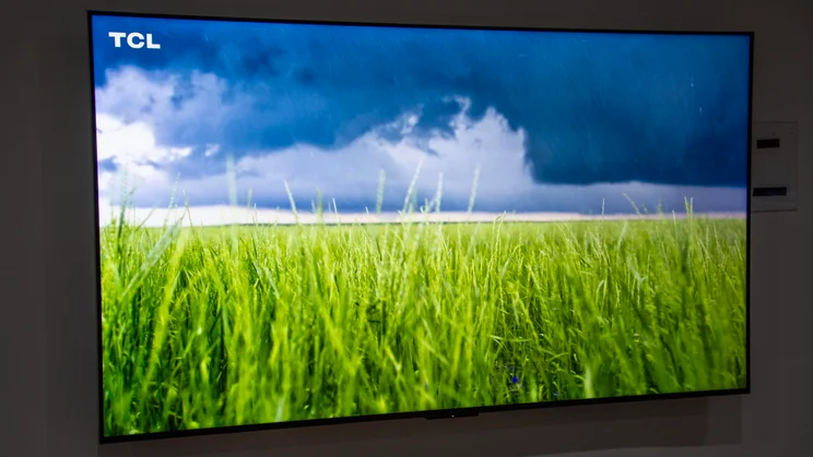 The TCL C7L SQD Mini LED TV mounted on a wall displaying a grassland scene with a storm on the horizon