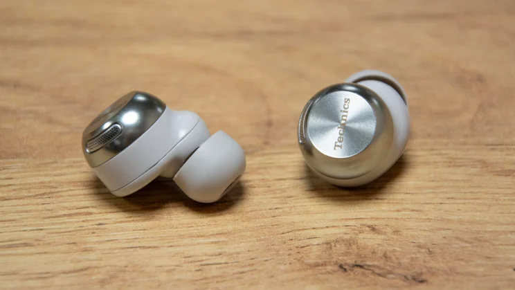 The Technics EAH-AZ100 wireless earbuds on a wooden table with one earbud turned inwards