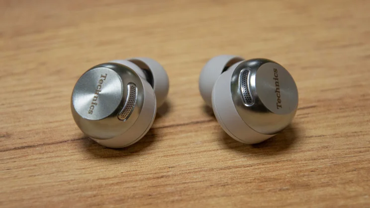 The Technics EAH-AZ100 wireless earbuds on a wooden table with their microphone array visible