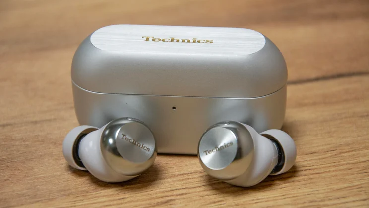 The Technics EAH-AZ100 wireless earbuds in front of their charging case on a wooden table