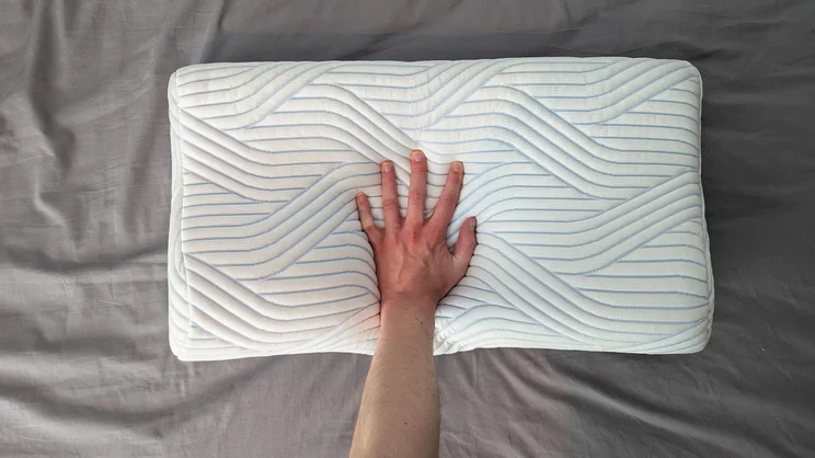The Tempur Original SmartCool Pillow on a bed, viewed from above, a hand pressing in the middle