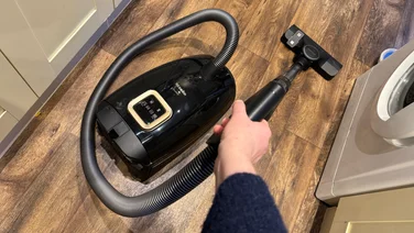 The Miele Guard L1 pictured vacuuming in a kitchen with a dark wood floor