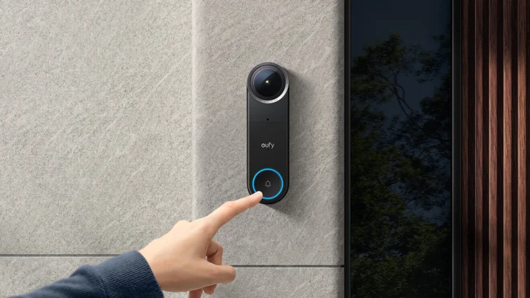 The Eufy Video Doorbell S4 mounted on a white rendered wall next to a dark wood door, modern architecture