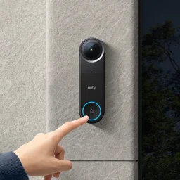 The Eufy Video Doorbell S4 mounted on a white rendered wall next to a dark wood door, modern architecture