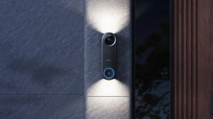 The Eufy Video Doorbell S4, at night, with night lights illuminated, mounted on a white rendered wall next to a dark wood door, modern architecture
