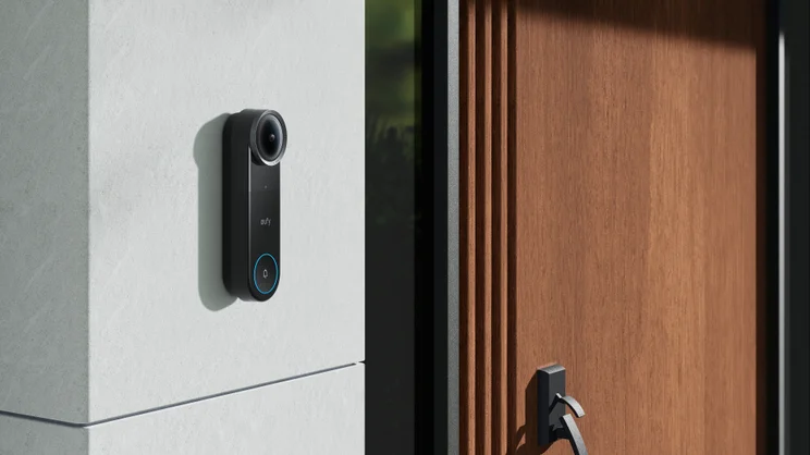 The Eufy Video Doorbell S4 mounted on a white rendered wall next to a dark wood door, modern architecture