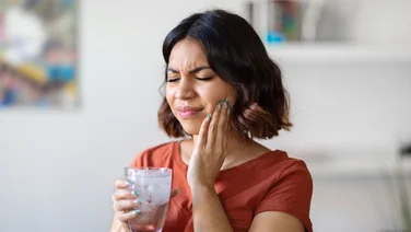 A young woman has a pained expression on her face as she drinks a glass of ice water