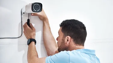 A handyman installing a security camera on a wall