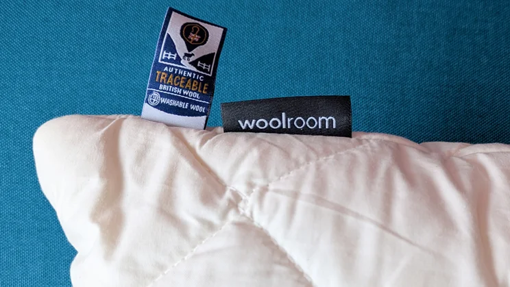 A closeup of the Woolroom Deluxe Washable Wool Pillow's corner, showing logo label and wool certification