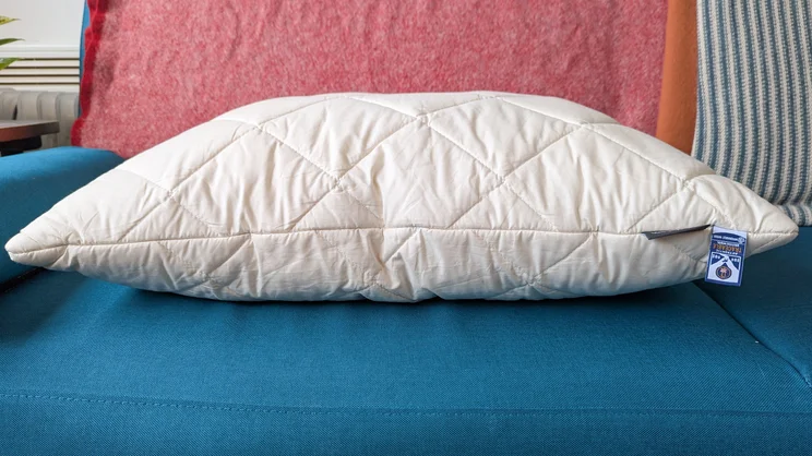 A side view of the Woolroom Deluxe Washable Wool Pillow, on a blue sofa