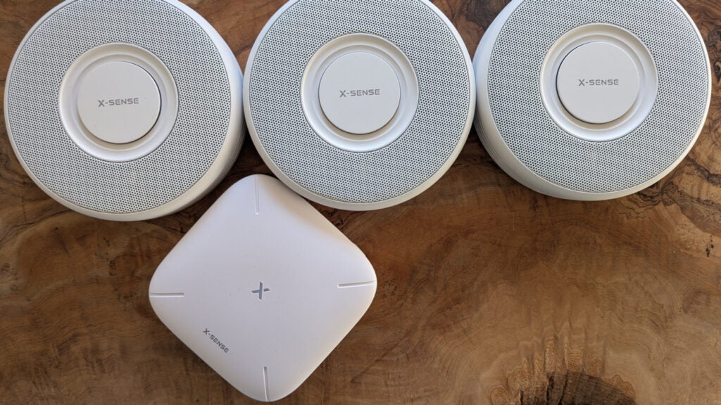 The X-Sense Link+ Pro smoke alarm system pictured in a group on a wood surface from above