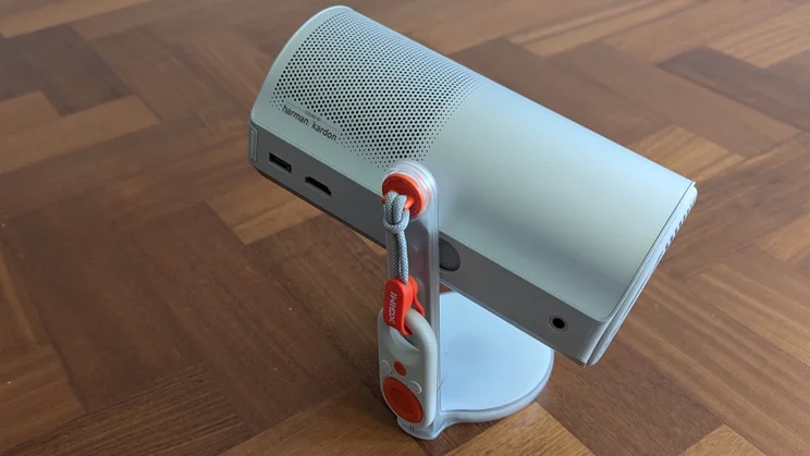 Side view of the XGIMI MoGo 4 Laser projector on a wooden floor with its mini remote attached to a lanyard