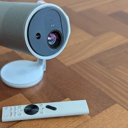 Front view of he XGIMI MoGo 4 Laser projector and its standard remote control on a wooden floor