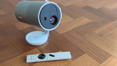 Front view of he XGIMI MoGo 4 Laser projector and its standard remote control on a wooden floor