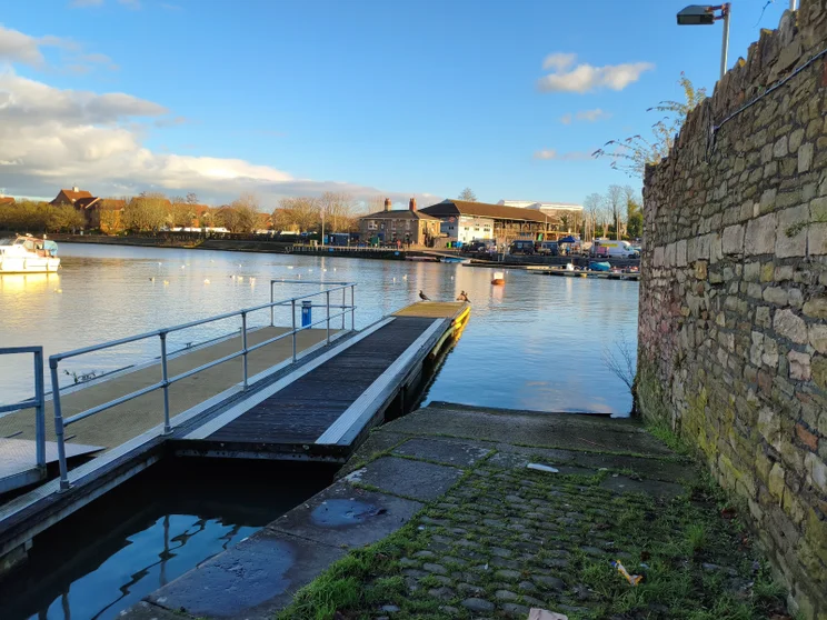 A dock leading onto a river, brick wall on the right