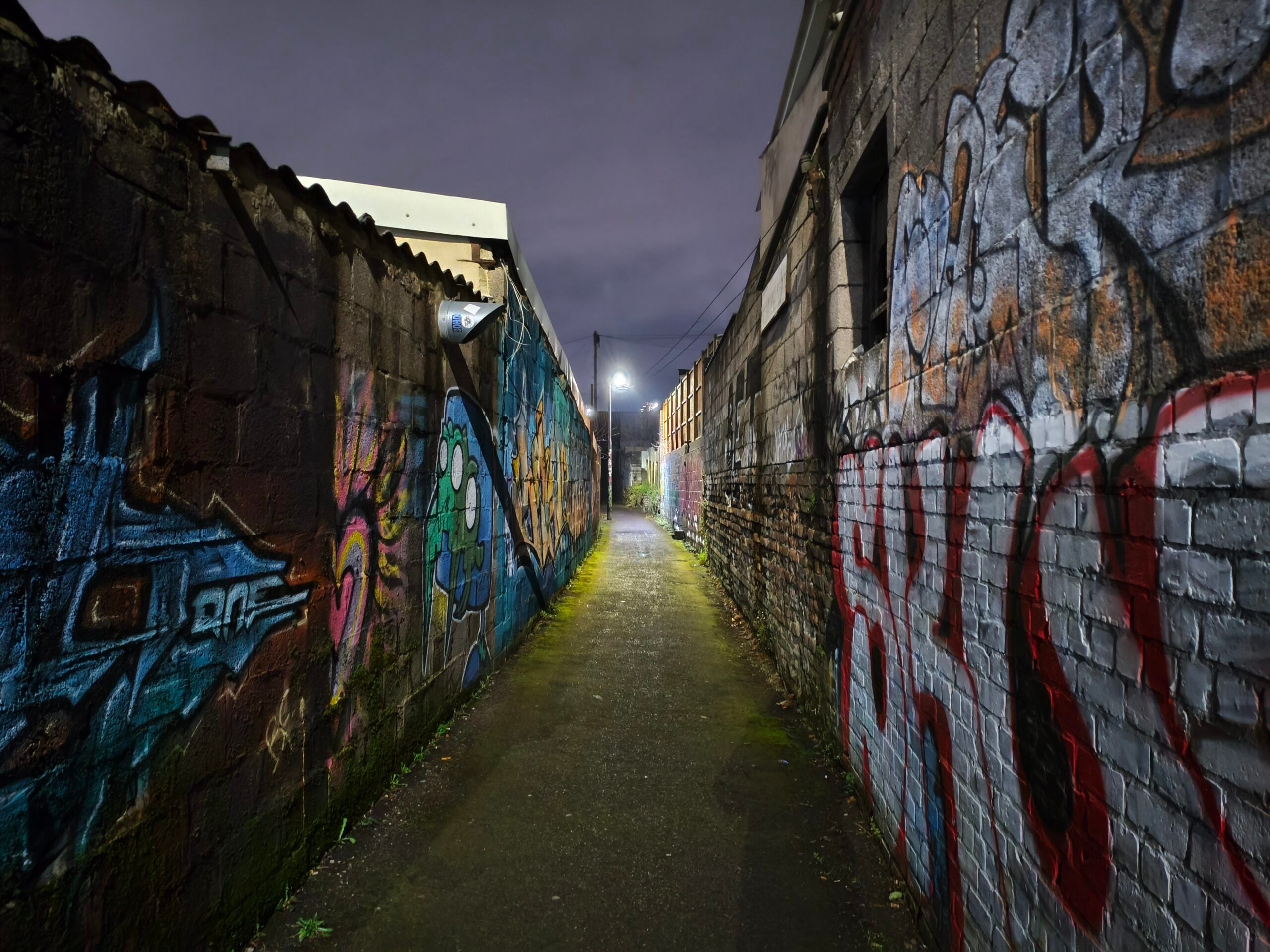 A dark alleyway at night, graffiti covering the walls on both sides