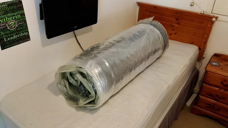 The Zoma Hybrid mattress rolled up in its plastic packaging