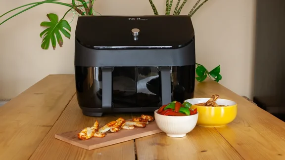 Image of an air fryer on a table with cooked vegetables and cheese
