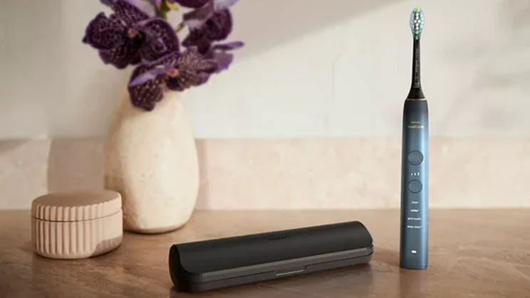 The Philips Sonicare DiamondClean 9000 standing on a tabletop, alongside its travel case and a vase of flowers